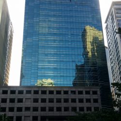 The tower of 88 Corporate Center has a facade made of blue glasses that forms a fork on the top. In the middle of the fork is a part of the building that has a concrete facade with small square windows. The lower levels of 88 Corporate Center on the side shown here is a podium structure on which the tower is mounted. The podium levels have several rectangular windows that seem to be open-air indicative of a parking level. However, the glass facade of the tower extends to the right side of the lower levels, and is partly seen in this picture.