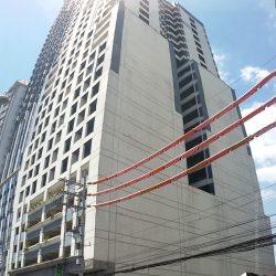 A vertical panorama of Annapolis Wilshire Plaza as seen from the sidewalk on the other side of Annapolis St. near its intersection with Columbia St. Its facade is white concrete with many square windows.