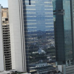 BPI Buendia Center has a tall rectangular prism shape with a trapezoidal prism on top. It features a concrete facade on the side face and a front face covered in dark glass panels. This picture was taken from the fifteenth floor of Citadel Inn Makati.