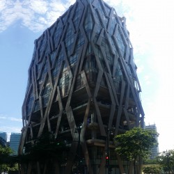 The floors of Clipp Center have an exterior covered with large transparent glass panels on the two lowest stories, open verandas for parking on the next three levels, and dark glass panels on the upper floors, all overlayed by diamond-shaped steel patterns. This is Clipp Center, as seen from the open parking area of KFC on the opposite corner.