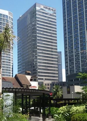 CyberOne Building, as seen from along the Orchard Road near its southern end that intersects with Eastwood Avenue. CybeOne is a gray high-rise building with alternating horizontal bands of concrete and glass windows. Decorative letters forming MEGAWORLD is near its top, just above the topmost glass row.