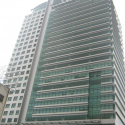 Gateway Tower is a gray rectangular prism with a concrete and glass facade and uneven divide. The larger part has bands of gray concrete and green glass panels, while the smaller part has small square windows. The photo was taken from the sidewalk along Gen. Malvar Ave. near Cambridge St.