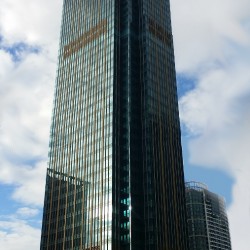 Metrobank Center is a tall rectangular prism covered with dark green glass. The top of the structure, which is a beige truncated pyramid, is barely visible from this shot taken from within the vacant lot surrounded by 35th St., 9th Ave., 34th St., and 8th Ave.