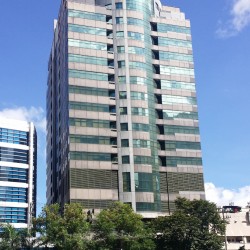 I-Square Building is a tall cuboid with a vertical semi-cylindrical protrusion in front. The upper floors have gray concrete and blue glass facade, while the lower floors have steel-covered windows. This is I-Square, as seen from the parking between Sapphire Road and Garnet Road near Julia Vargas Avenue.