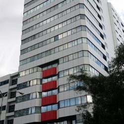 The Jollibee Centre, as seen from the sidewalk on the opposite side of San Miguel Avenue. The building is blocky in shape and has rows of concrete walls and glass windows.