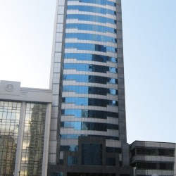 Multinational Bancorporation Centre is a tall rectangular prism with a facade of alternating bands of gray tiles and dark glasses on the upper floors and black tiles on the lower floors. The picture was taken from within the car park along Ayala Avenue on the opposite side. The adjacent LKG tower was edited to make Multinational Bancorporation Centre stand out.