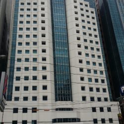 The exterior of the Octagon Center is white concrete with several small square windows and a continuous section of vertical glass panels in the middle. This picture was taken from the Petron gasoline station across San Miguel Ave.