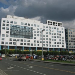 One E-com Center is one low-rise building that looks like two separate buildings, a white rectangular one and a gray square; both have concrete exteriors and several small square windows. This is One E-com Center as seen from Palm Coast Dr. cor. Seaside Blvd.