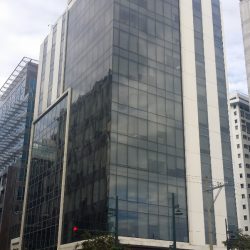 One Orion Tower as seen from the sidewalk on the opposite corner: 11th Ave. and 38th St. It has mostly glass facade with some white concrete wall parts.