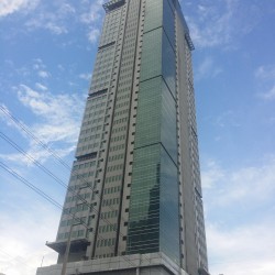 One San Miguel Building is a tall vertical structure with a facade of concrete and glass panels. This picture was taken from the opposite corner at Sheridan St. cor. Shaw Boulevard.