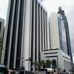 Busy street with cars in front of tall, modern buildings under a partly cloudy sky. Pacific Star building, the one in front, as seen from front of RCBC Makati Ave. branch (Makati Ave. cor Buendia). The buildings BPI Buendia Center and Petron Megaplaza (right) and BDO Corporate Center (left).