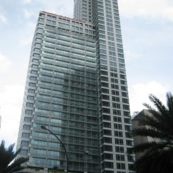 High-rise building with glass facade and red logo at the top, flanked by palm trees.