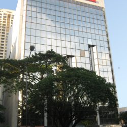 The low-rise building is almost square and has an exterior made of glass panels. This is the view from the sidewalk on the other side of Paseo De Roxas, indirectly across it (directly across the Paseo Center).