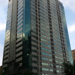 The Prestige Tower is a tall rectangular prism with an exterior of gray concrete, dark green glass panels, and dark gray marble near the entrance. This is the building, as seen from the sidewalk on the opposite side of Emerald in front of the Orient Square.