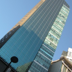 Robinsons Summit Center has tall rectangular shape, with a smaller triangular prism extension and a facade of teal glass panels. Picture of Robinsons Summit Center taken from the sidewalk in front of Security Bank Centre on the other side of Ayala Avenue.