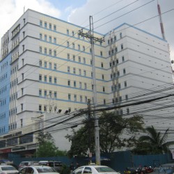 Sunnymede IT Center has a facade of mainly white concrete with small windows. Its structure has an L-shaped cross-sectional area. This is the view from the island dividing Quezon Ave. directly in front of the Triumph Building.