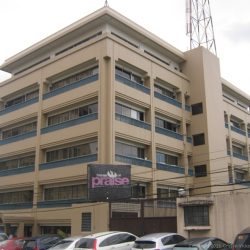 Sysu Centre standing as seen from the front of Cacao Hotel on the opposite side of Sgt. Esguerra St. Sysu Centre is a beige blocky low rise building with dark gray railings and glass windows from the second to the fifth floor. The ground floor has larger glass windows flanking the main entrance. The top floor has smallar area and recessed inward as if it's a penthouse. OPn the right side is a rectangular shaft that runs from ground to top floor, probably an elevator shaft.